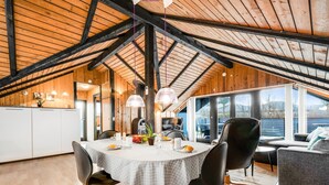 A spacious dining area with a round table, black chairs, and a wooden ceiling.