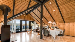 A spacious loft with a high ceiling, wooden beams, a dining area with a table and chairs, and a large sliding glass door leading to an outdoor patio.