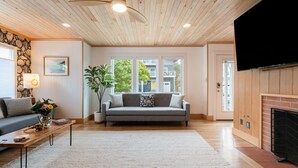 A living room with a wooden ceiling, a grey sofa, a coffee table, and a fireplace. - Cove Beach Retreat • Fire Pit + Golf Course Nearby | Grey Oak (Seaside)