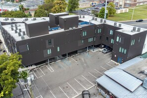 A multi-story building with a parking lot, air conditioning units, and a blue roof section.