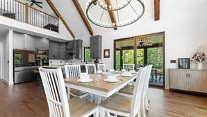 Eine geräumige Küche mit modernen Geräten, ein Essbereich mit weißen Stühlen und eine große Chandelier.