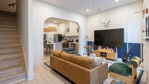 Una sala de estar moderna con un sofá, una mesa de centro, un televisor y una cocina al fondo.