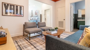 A modern living room with two grey armchairs, a blue sofa, and a coffee table. There is a large mirror on the wall and a framed artwork above the fireplace. - The Conway | Ensemble Escape in DT Nash | 5 Bdrs (Nashville)