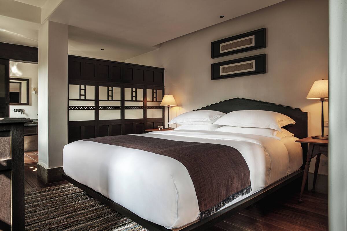A large bed with a dark headboard, two bedside lamps, and a wooden headboard with a mirror.