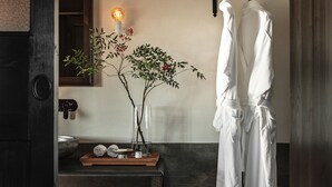 A bathroom with a wooden bench, a mirror, a vase with a branch, and two white robes hanging on a rack. - Dali Ancient Town Anyu Hotel (Dali)