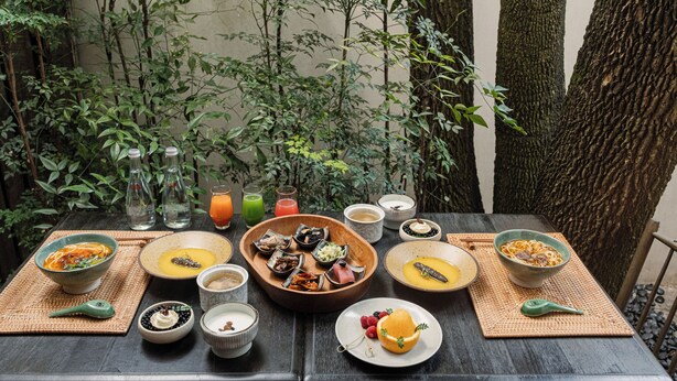 A table set with various dishes and drinks, surrounded by greenery and trees. - Dali Ancient Town Anyu Hotel (Dali)