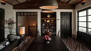 A dining area with a long table, chairs, a bowl of fruit, a potted plant, and a bookshelf with various items. - Dali Ancient Town Anyu Hotel (Dali)