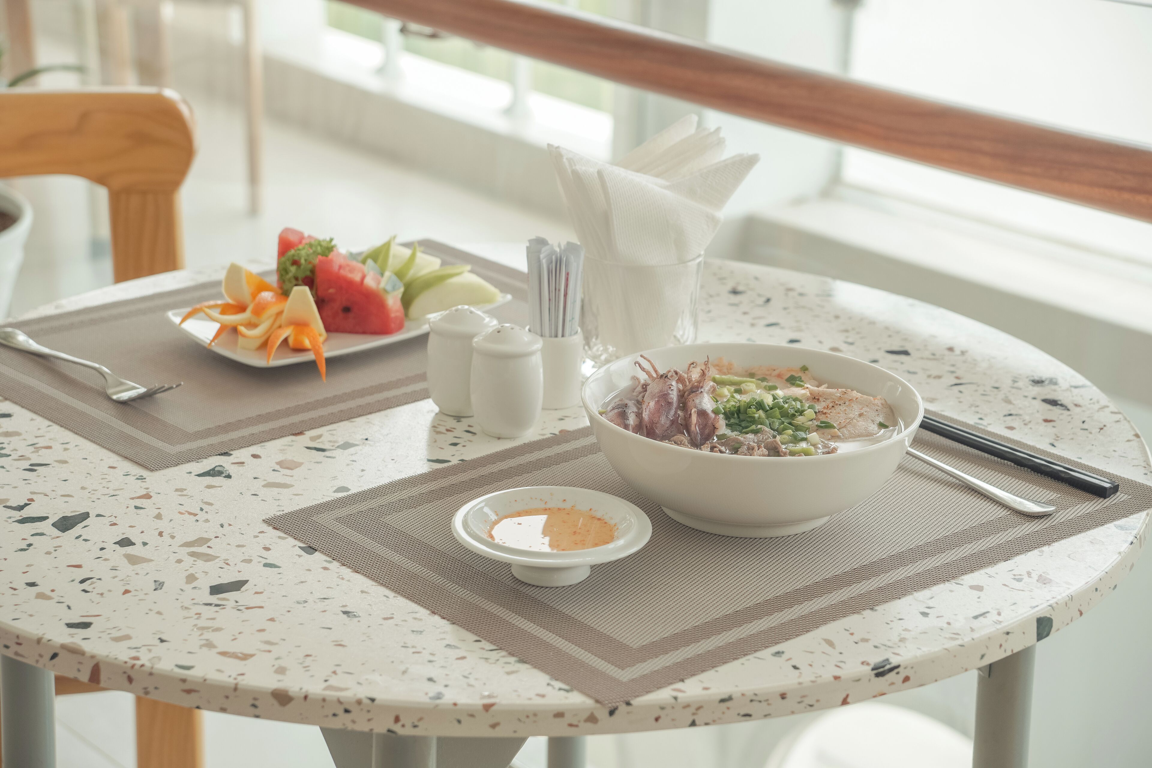 A dining table with a bowl of soup, a plate of vegetables, and condiments.