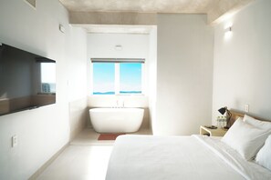 A modern hotel room with a large bed, a built-in bathtub, and a view of the ocean. - The Up Hotel Phu Quoc Island - The Poolside Escape (Phu Quoc)