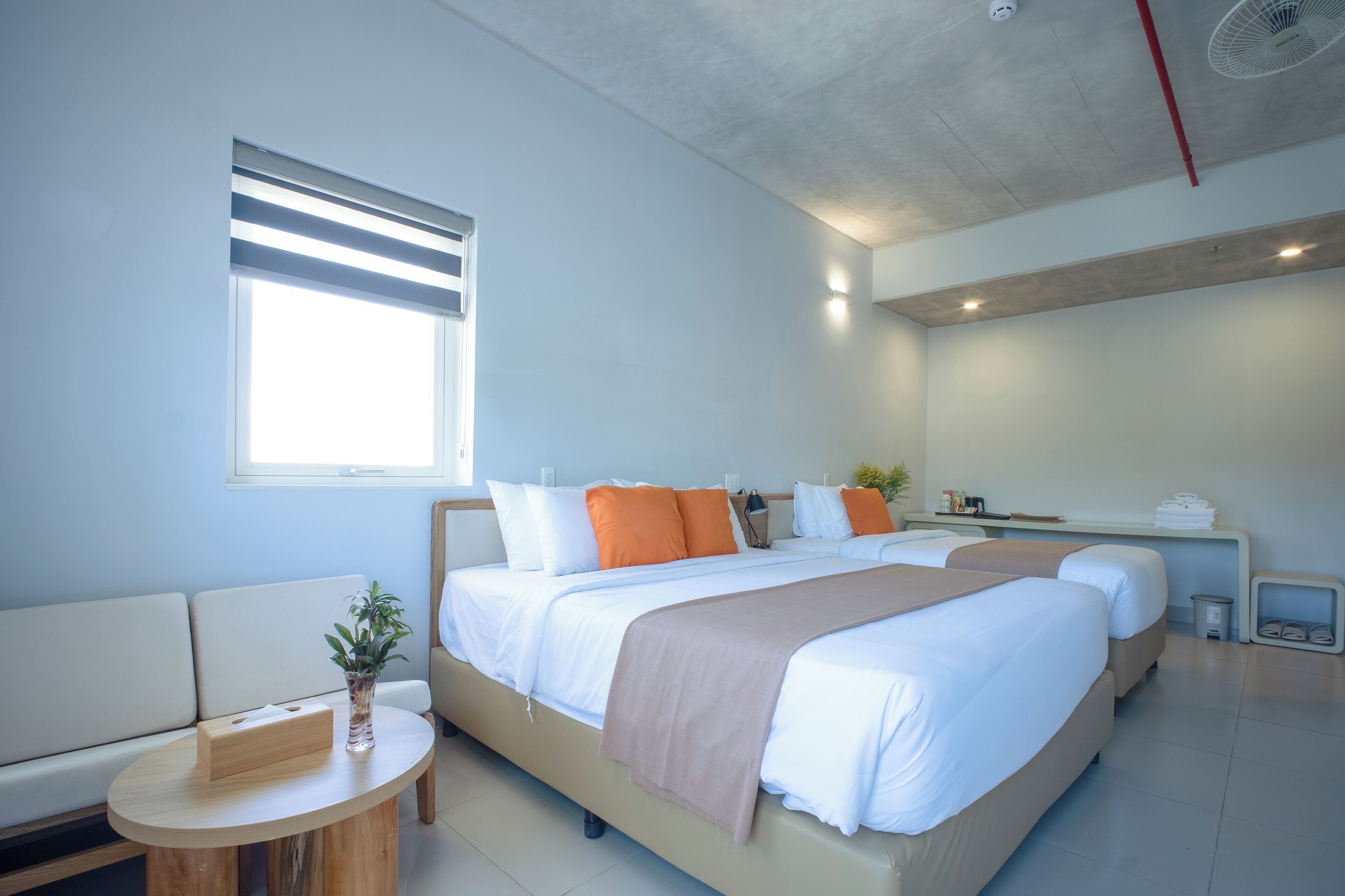 Et moderne hotelværelse med en stor seng, et sengebord, et lille rundt bord og et vindue med persienner.