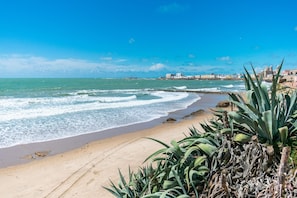 A beach with waves, a clear sky, and buildings in the distance. - Holiday Home in Cadiz by the Sea (Cadiz)