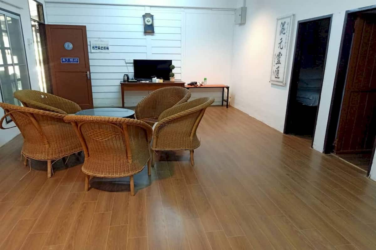 A room with a wooden floor, a round table with four wicker chairs, a television on a stand, and a door with a sign.