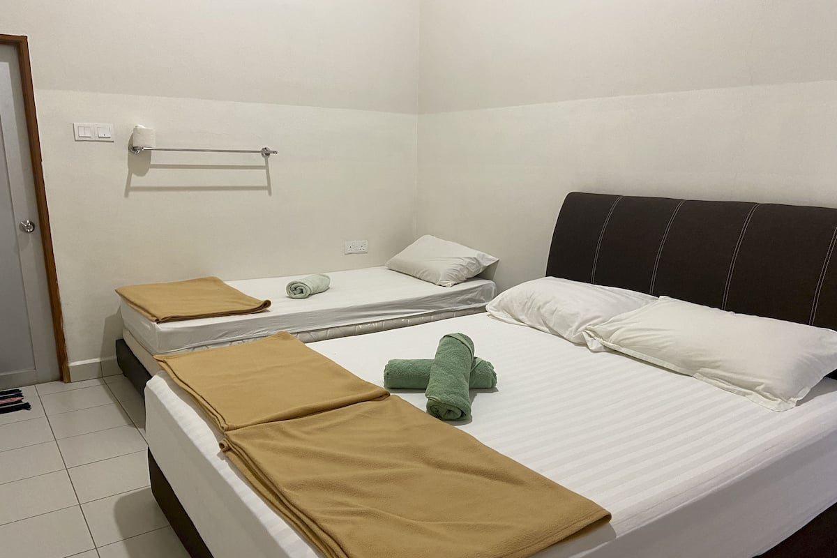 A hotel room with two beds, each with a white mattress and brown blankets. There is a green towel on the floor between the beds.