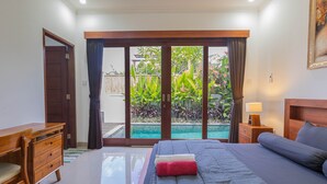 Un dormitorio con cama, escritorio, mesita de noche y vistas a una piscina y jardín.
