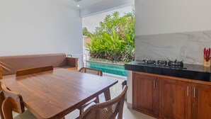 Una cocina moderna con una mesa y sillas de madera, una estufa empotrada y vistas a un jardín con plantas y una piscina.