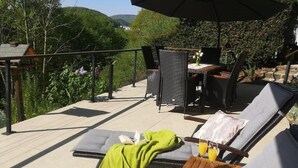 Een terras met lounge fauteuils en een tafel, omringd door groen en uitzicht op heuvels.