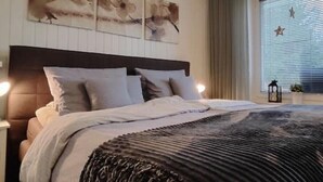 Een slaapkamer met een bed, hoofdeinde, nachtkastje, raam met jaloezieën en wanddecoratie.