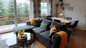 A modern living room with a dark grey sofa, a round coffee table, and a dining area with a white table and black chairs.