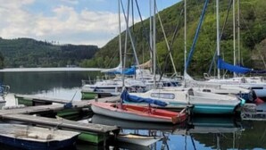 A marina with several boats docked, surrounded by a calm lake and a forested hillside.