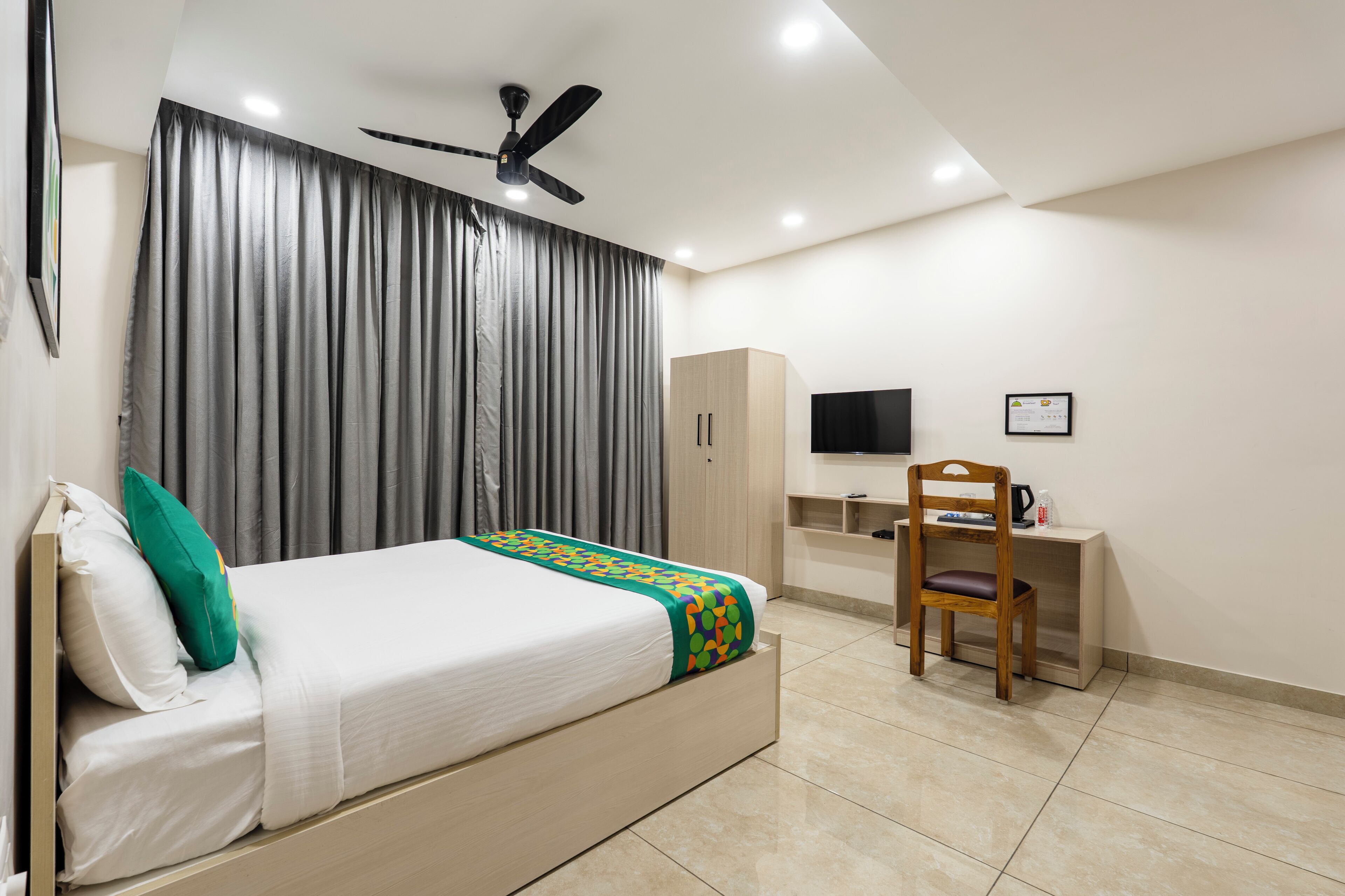 A bedroom with a bed, a desk, a chair, a wardrobe, and a ceiling fan.