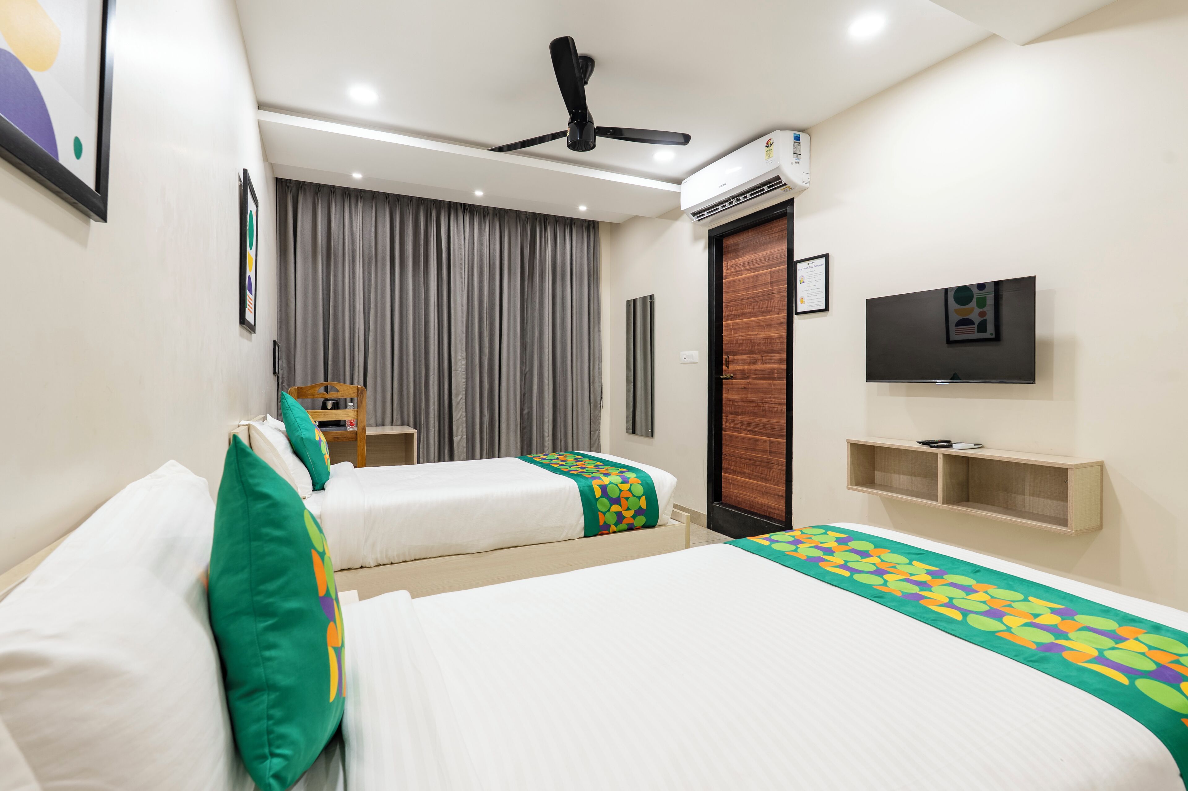 A hotel room with two beds, a ceiling fan, an air conditioner, a TV, and a wooden door.