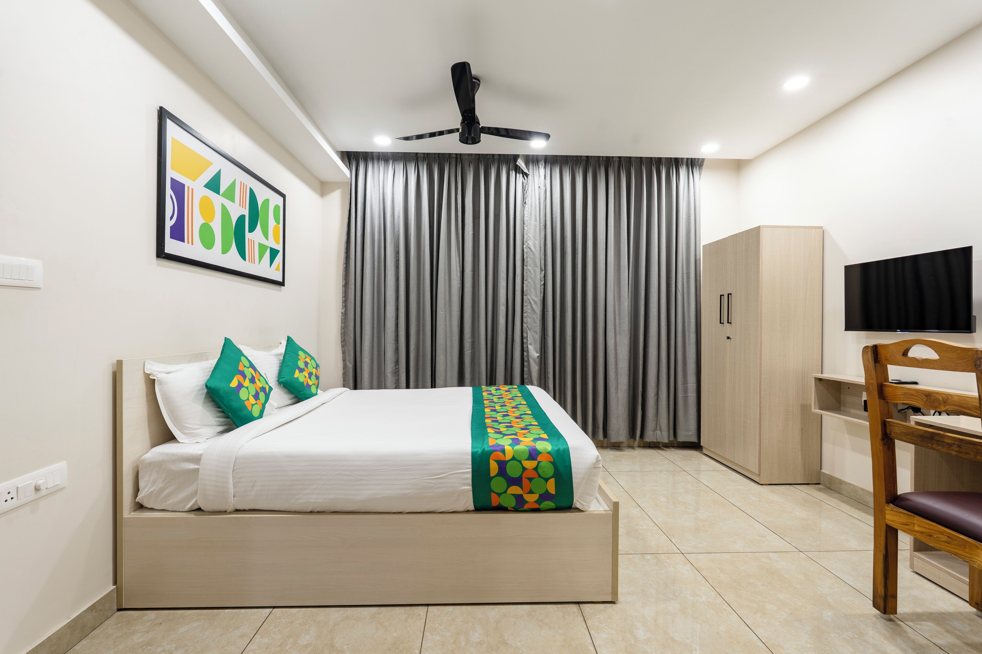 Une chambre d’hôtel moderne équipée d’un lit, d’un bureau, d’une chaise, d’une télévision et d’un ventilateur de plafond.