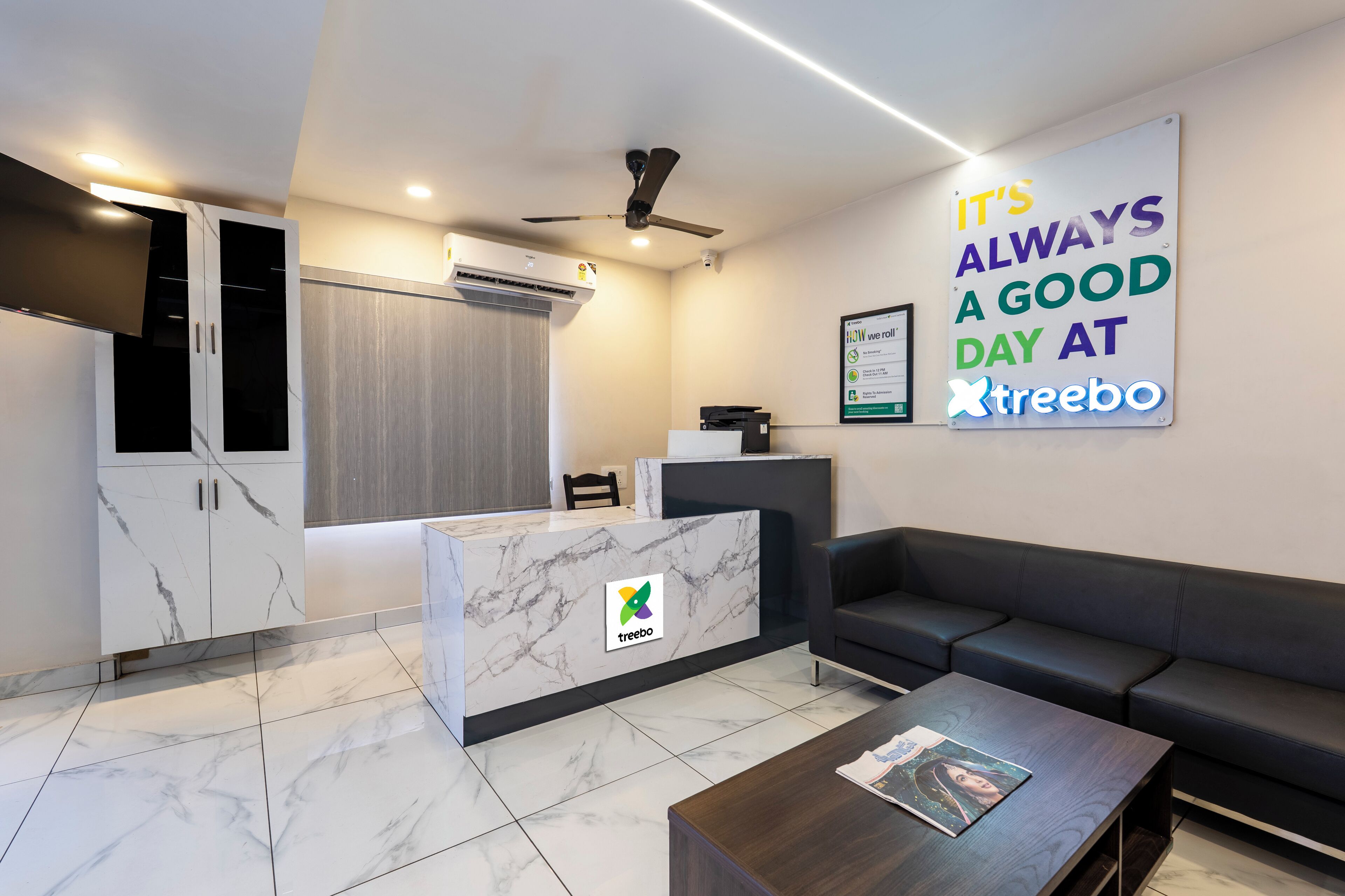 A modern reception area with a marble reception desk, a black leather sofa, and a ceiling fan.