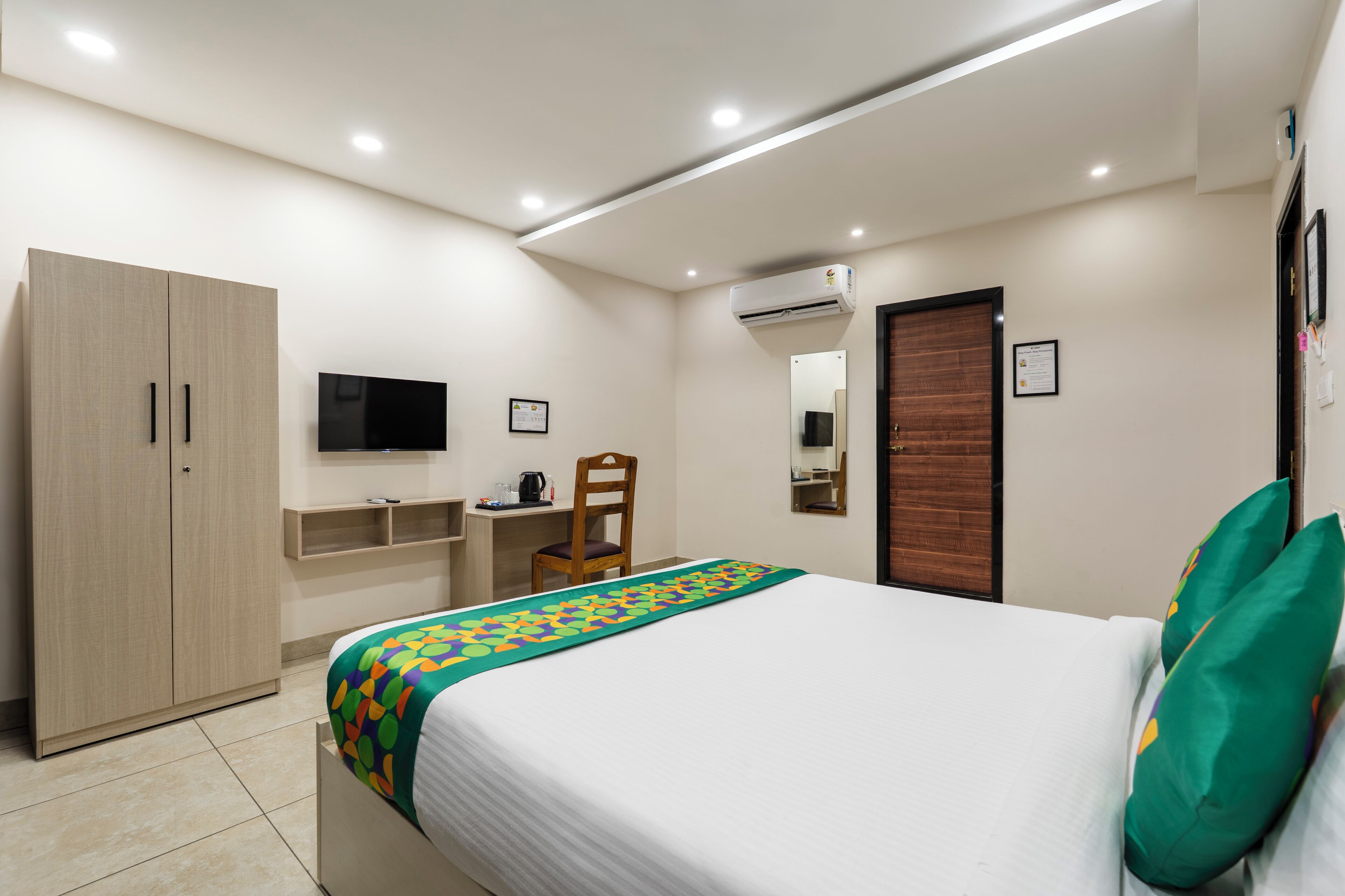 A bedroom with a bed, a desk, a chair, a wardrobe, a TV, and an air conditioning unit.