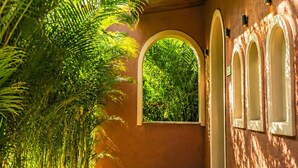A hallway with a wooden ceiling, a window with a view of greenery, and a wall with arched niches.