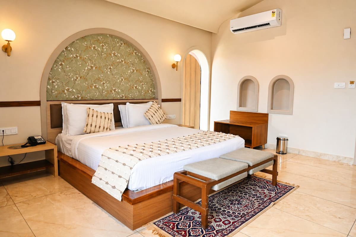 A hotel room with a bed, bedside table, lamp, and an air conditioning unit.
