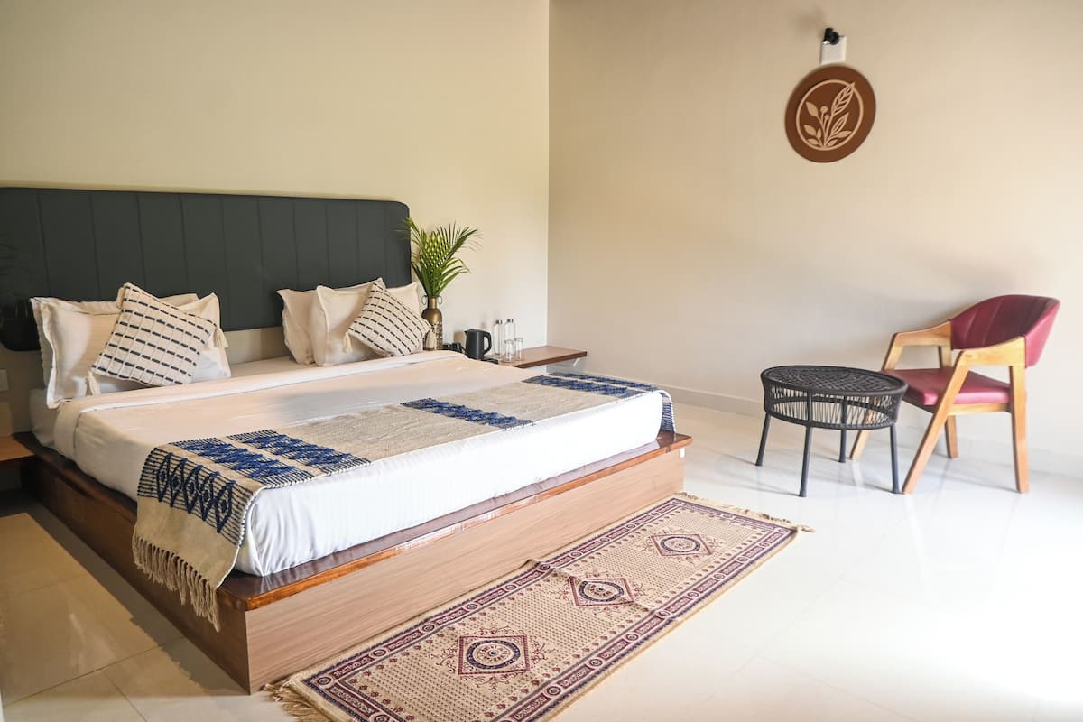 A bedroom with a bed, a chair, a small table, a wall decoration, and a plant.