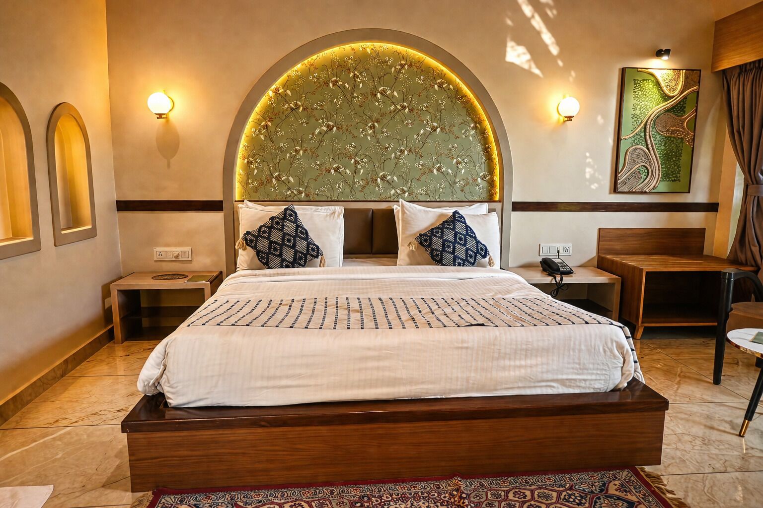 A hotel room with a large bed, two bedside tables, a desk, a chair, and a decorative wall piece.