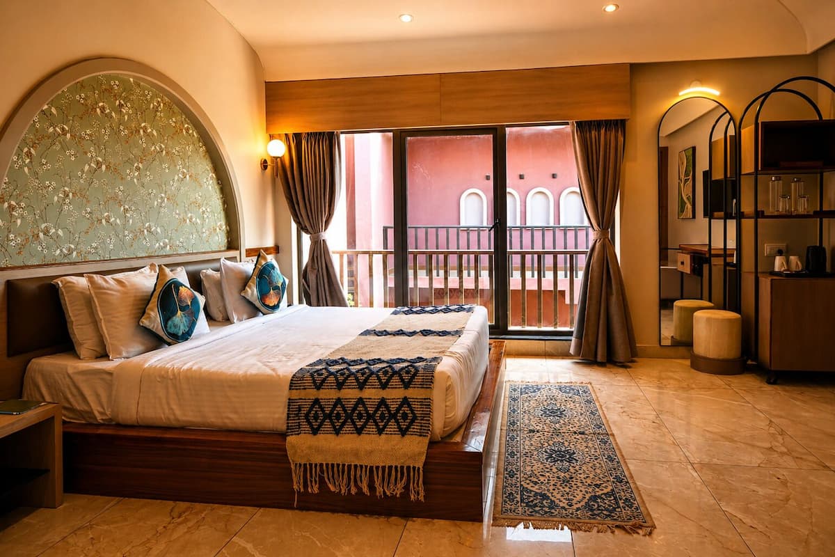 A hotel room with a large bed, a balcony with a view, a small desk, and a mirror.