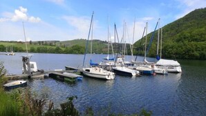 A marina with several sailboats docked, surrounded by greenery and hills.