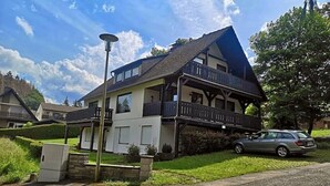 A two-story house with a balcony, a car parked in front, and a street lamp nearby.