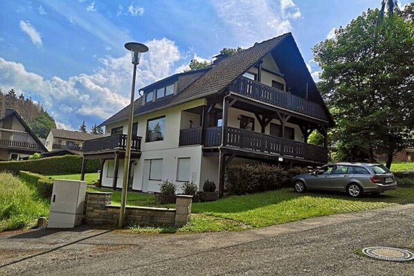 A two-story house with a balcony, a car parked in front, and a street lamp nearby.