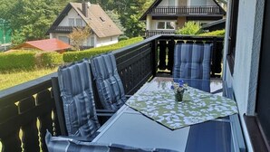 A balcony with a glass table, blue striped cushions, and a floral tablecloth.