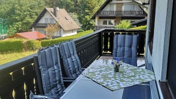 Un balcón con una mesa de vidrio, cojines azules a rayas y un mantel con motivos florales.