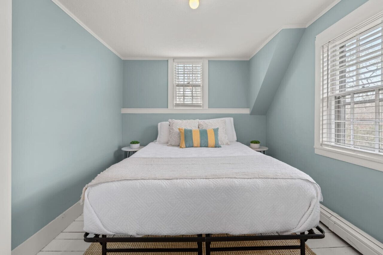 A bedroom with a bed, two bedside tables, and a window with blinds.