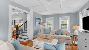 Un salon avec un canapé, une table basse et un téléviseur. Un escalier mène à une autre pièce.