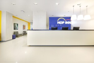 Uma área de recepção de hotel com balcão, espaço para sentar e uma grande placa azul com o nome do hotel.