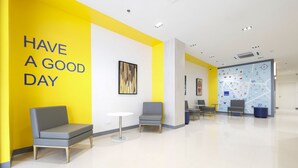 A modern lobby with a bright yellow accent wall, a seating area with chairs and a small table, and a map on the wall.