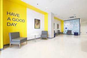 Um lobby moderno com uma parede de destaque amarelo vibrante, uma área de estar com cadeiras e uma mesa pequena, e um mapa na parede.