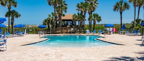 A swimming pool with lounge chairs and umbrellas, surrounded by palm trees.