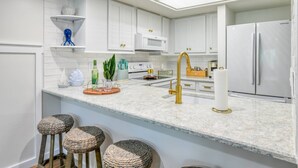 A modern kitchen with white cabinets, a stainless steel refrigerator, a gold faucet, and a marble countertop. - Beach Views, 2 Balconies, Beach Access, 2 Pools 1 Heated, 5 miles to Downtown, $300 in Free Tickets! (St. Augustine)