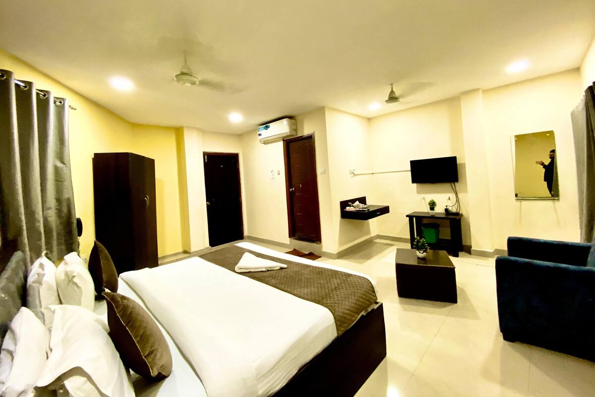 Habitación de hotel con cama, escritorio, silla, televisión y espejo.