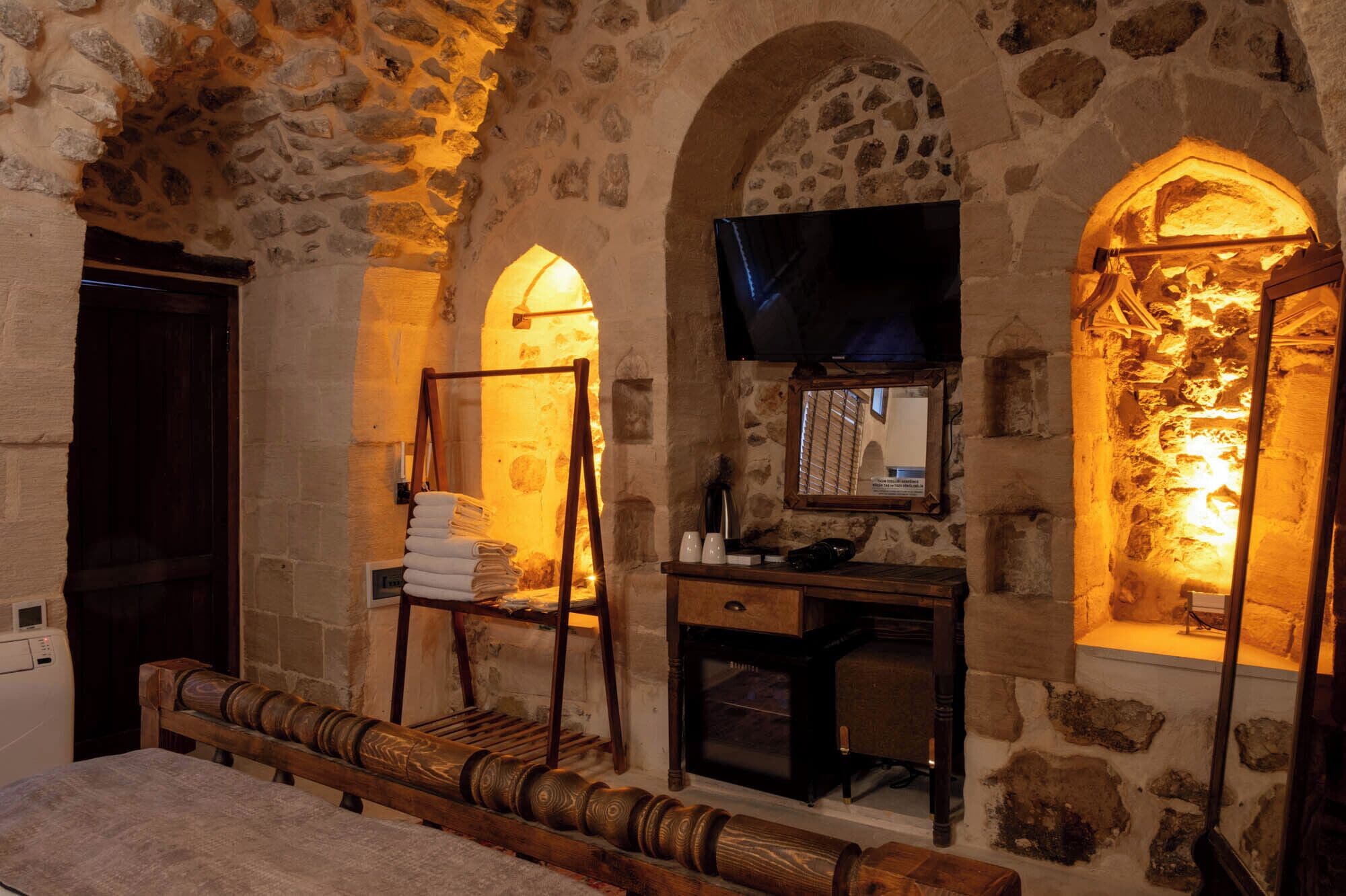 A stone-walled room with a wooden bench, a TV mounted on the wall, and a small table with towels.