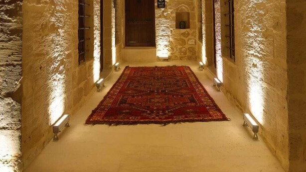 A corridor with a patterned carpet, stone walls, and a wooden door at the end. - Marvel Otel (Mardin)