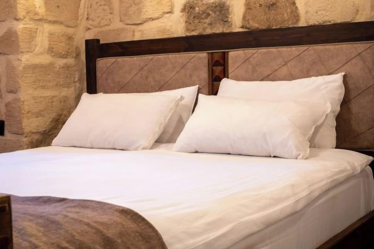 A bed with white linens and a wooden headboard in a room with stone walls.