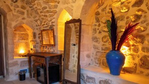 A stone-walled room with a wooden vanity, a mirror, and a vase with decorative feathers. - Marvel Otel (Mardin)